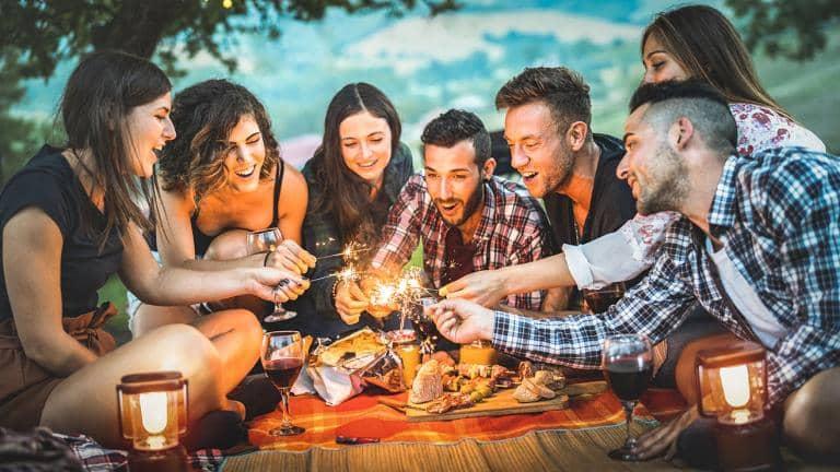 A group of young people enjoying an alfresco picnic and lighting sparklers